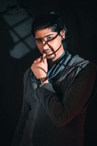 Young man looking away while standing against black background