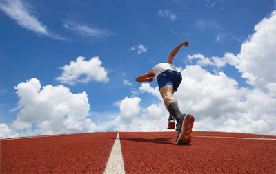 Low angle view of man running against blue sky