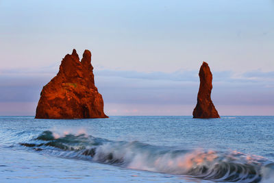 Rocks in sea against sky during sunset