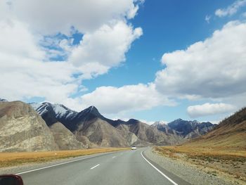 Empty road leading towards mountains against sky