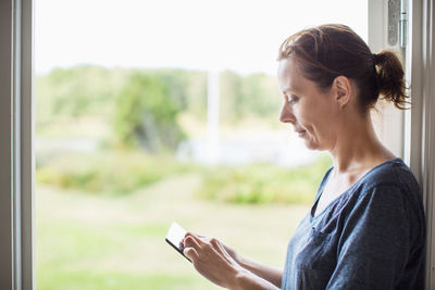 Side view of woman using digital tablet by window at home