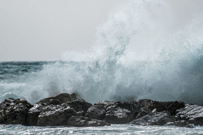 Waves splashing on rocks against sky