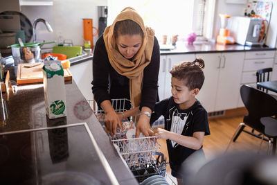 Mother and son arranging utensils in dishwasher at kitchen