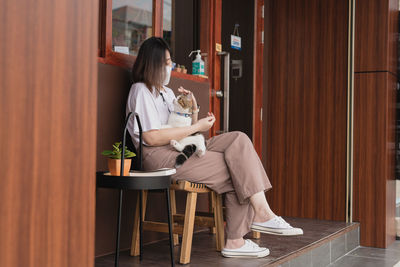 Asian woman wearing protective mask sit and play with her cat at outdoor coffee shop