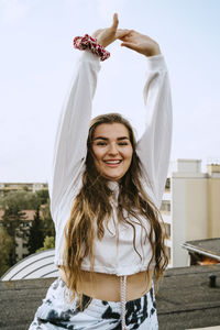 Portrait of smiling woman with arms raised practicing yoga on rooftop