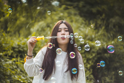 Young woman blowing bubbles against plants