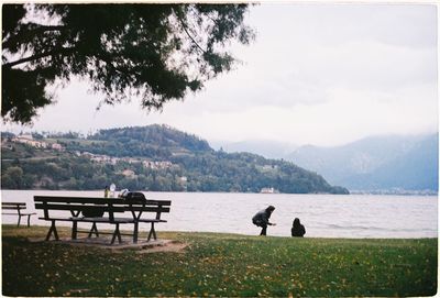 Rear view of people on bench by lake against sky