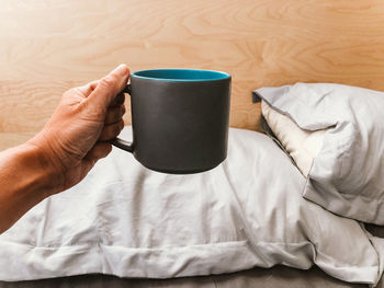 Midsection of womans hand holding coffee cup on bed