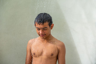 Shirtless man taking shower against wall