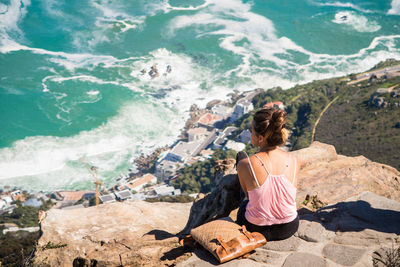 Rear view of woman looking at sea while sitting on cliff