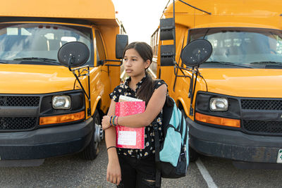 Young hispanic girl standing in between school buses after school