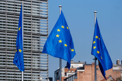 Low angle view of flags against buildings against blue sky