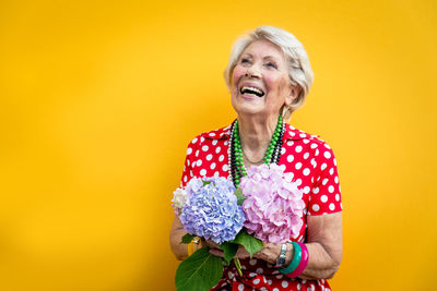 Senior woman holding flower standing against colored background