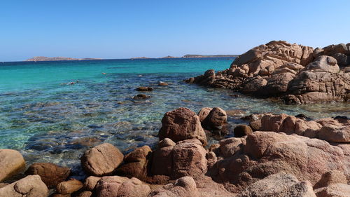 Scenic view of rocks in sea against clear blue sky