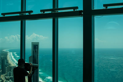 Rear view of man looking at sea through window