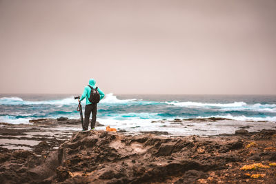 Rear view of man standing at beach against sky