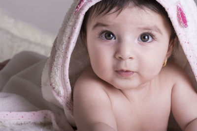 Close-up portrait of shirtless baby girl lying on bed