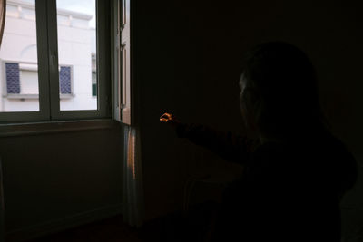 Side view of man looking through window at home