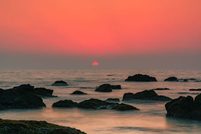 Rocks in sea against romantic sky at sunset