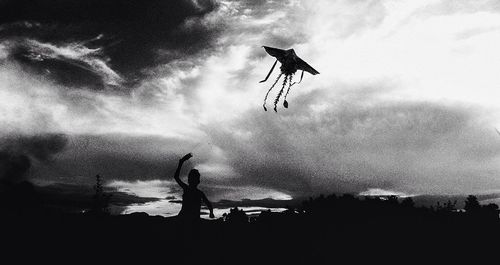 Low angle view of silhouette man paragliding against sky