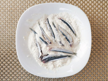 Directly above shot of anchovies on flour in plate at table