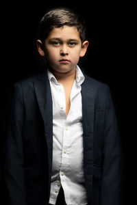 Portrait of boy wearing blazer standing against black background