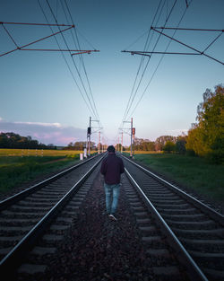 Rear view of person walking on railroad track against sky