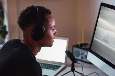 Young freelance worker wearing headphones podcasting in front of computer