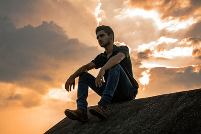 Low angle view of young man sitting against sky during sunset