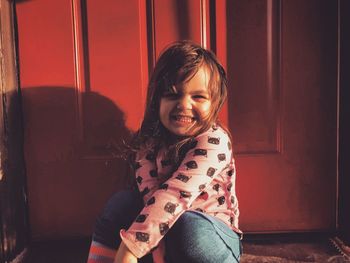 Portrait of cute smiling girl sitting at doorway