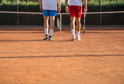 Low section of male friends playing tennis on court