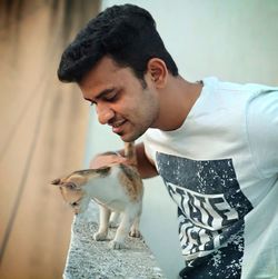 Close-up of young man looking down while holding kitten on retaining wall