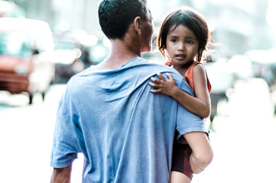 Rear view of father carrying daughter on road