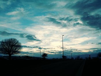 Road by silhouette trees against sky at sunset