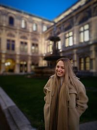 Portrait of smiling young woman standing against building