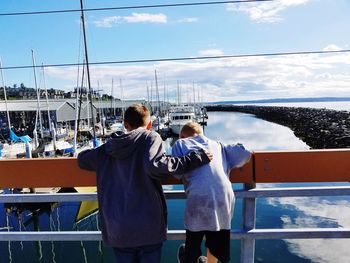 Rear view of brothers looking at sea while standing by railing against sky during sunny day