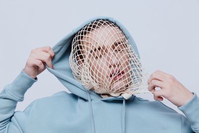 Young man wearing hooded shirt standing against white background