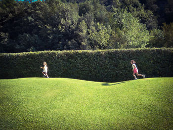 Sisters running on field against trees