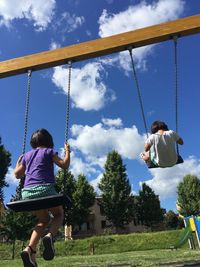 Children playing on swing at playground against sky