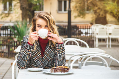 Thoughtful young woman having dessert with coffee at outdoor cafe