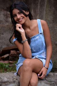 Portrait of smiling woman sitting on retaining wall