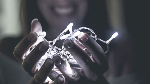 Midsection of mid adult woman holding illuminated string lights in darkroom