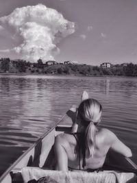 Rear view of woman sitting in boat on lake against sky