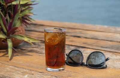 Close-up of cold drink by sunglasses on table outdoors