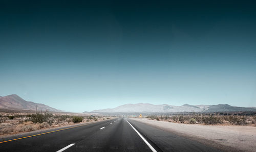 Empty road along landscape and mountains against clear sky