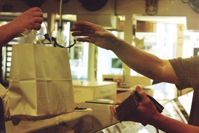 Cropped image of shopkeeper giving bag to customer in store