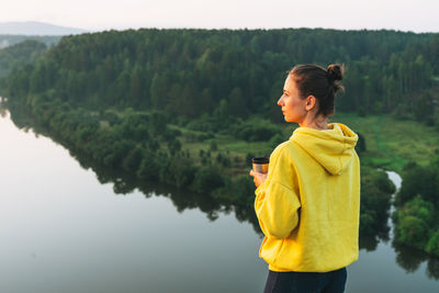 Young woman girl traveler in yellow hoodie with cup of the morning coffee looking at sunrise on 