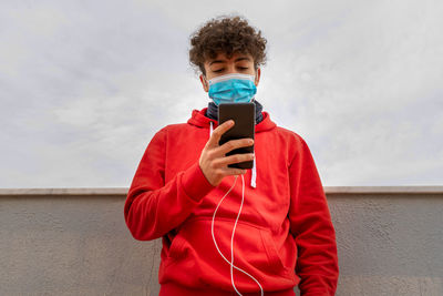 Man holding smart phone while standing against wall