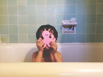 Boy with toy taking bath in tub at home