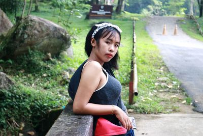 Portrait of young woman standing by railing at roadside